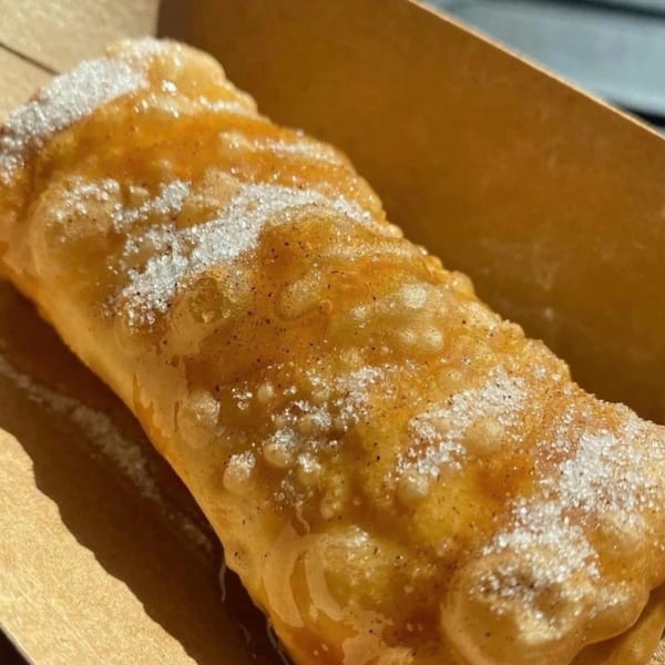 Close-up of a golden-brown Blasian Fusion dessert, drizzled with syrup and sprinkled with sugar.