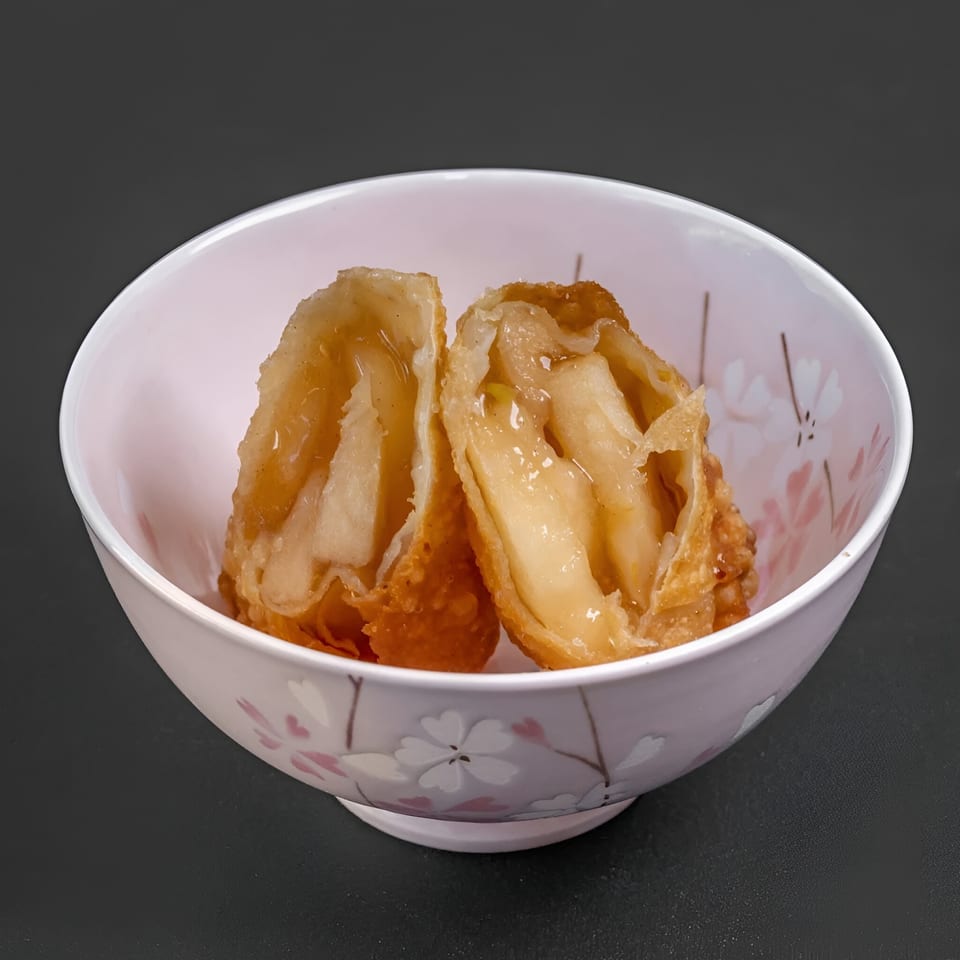 Two Blasian Fusion apple pie egg rolls, cut open, in a white bowl with pink cherry blossoms.