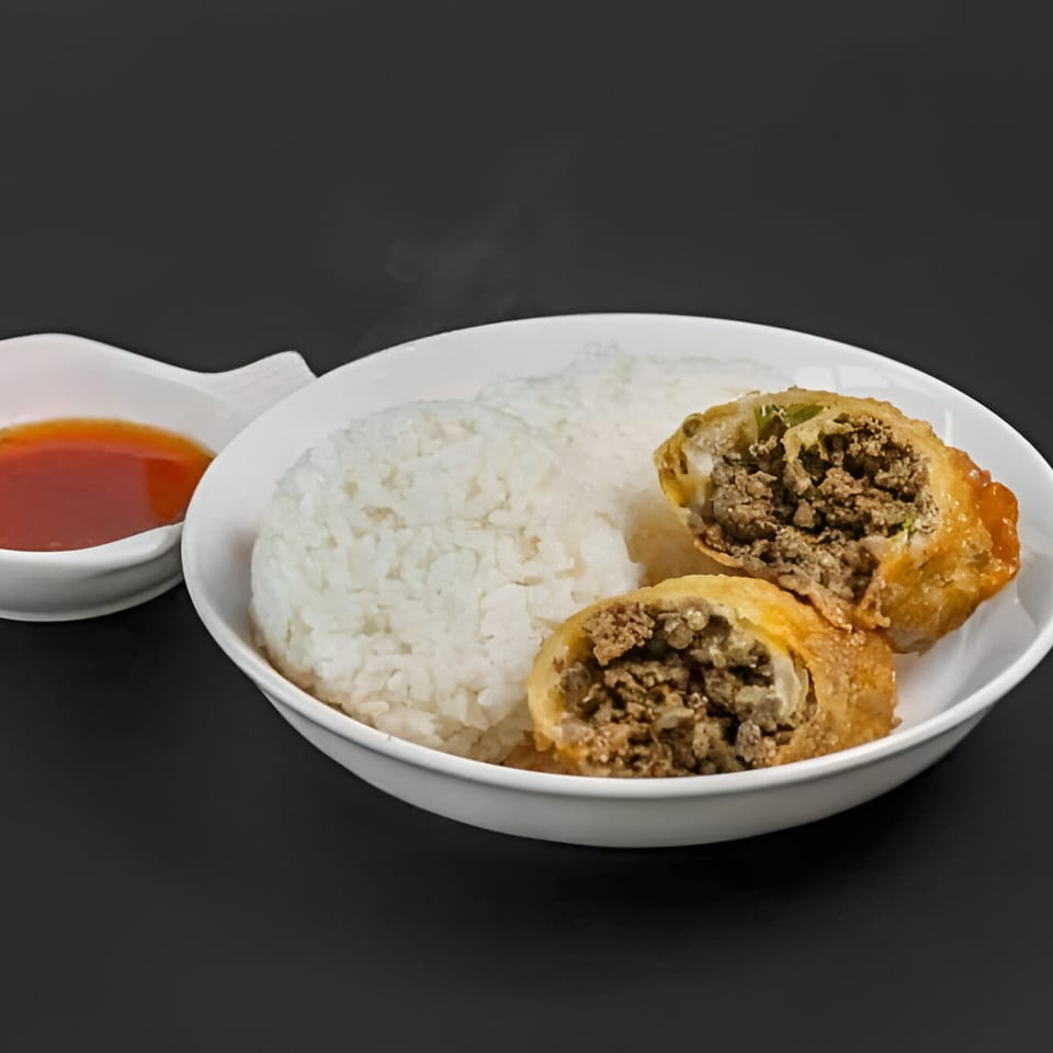 Steaming white rice with two crispy Blasian Fusion egg rolls, filled with ground meat, and a side of dipping sauce.