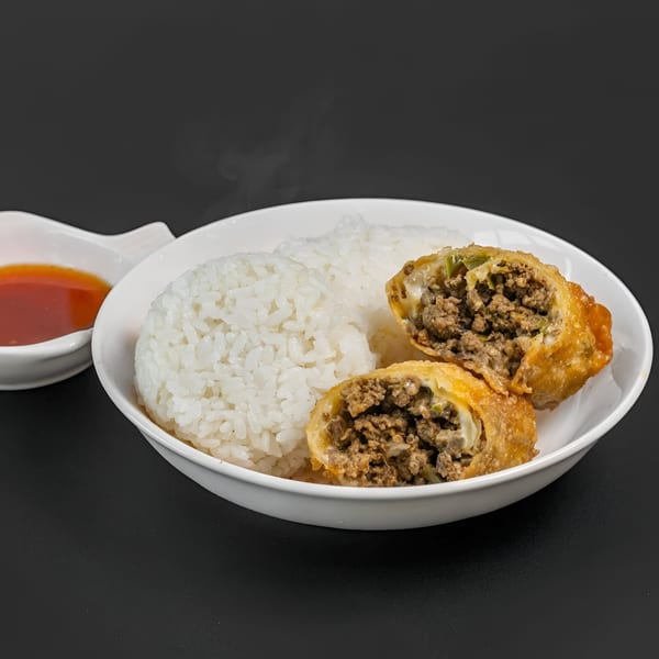 Steaming white rice and two crispy, cut egg rolls filled with ground meat, served with dipping sauce.