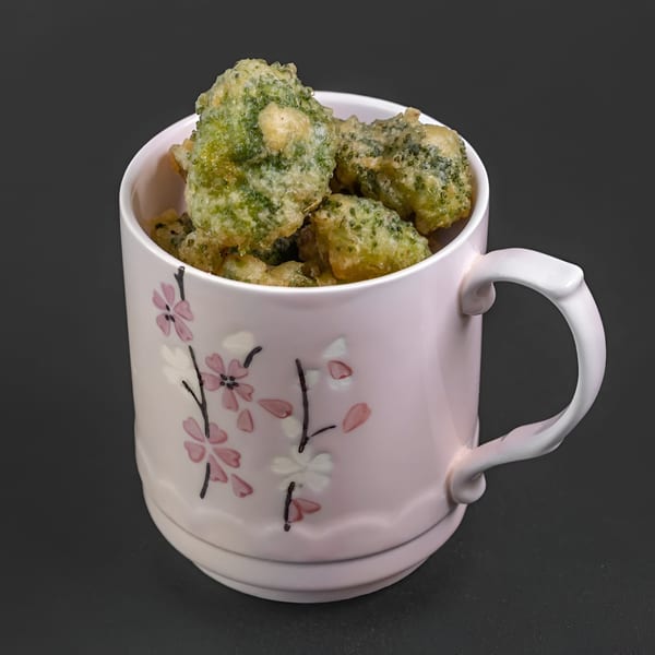 Tempura broccoli florets served in a pink mug with cherry blossom designs, against a dark background.