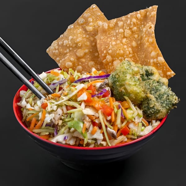 Blasian Fusion's Asian slaw with crispy wontons, tempura broccoli, and chopsticks in a black bowl.