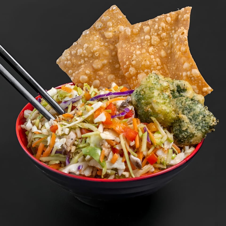 Blasian Fusion's Asian slaw with crispy wontons, tempura broccoli, and chopsticks in a black bowl.