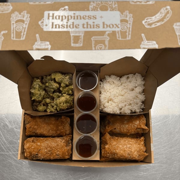 An open Blasian Fusion takeout box with fried chicken, rice, egg rolls, and dipping sauces.