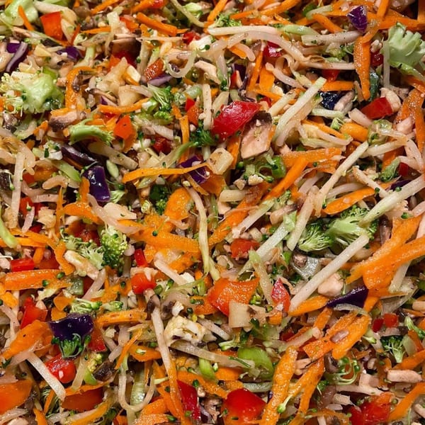 Close-up of a colorful Blasian Fusion salad with shredded carrots, broccoli, red peppers, and mushrooms.